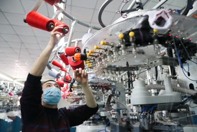 An employee wearing a face mask works on a production line manufacturing socks for export at a factory in Huzhou