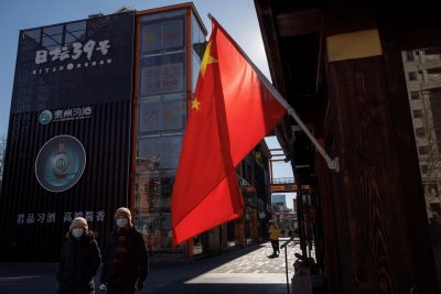 People walk past the Chinese national flag as the coronavirus disease (COVID-19) outbreak continues in Beijing, China, 13 January 2022 (Photo: Reuters/Thomas Peter).